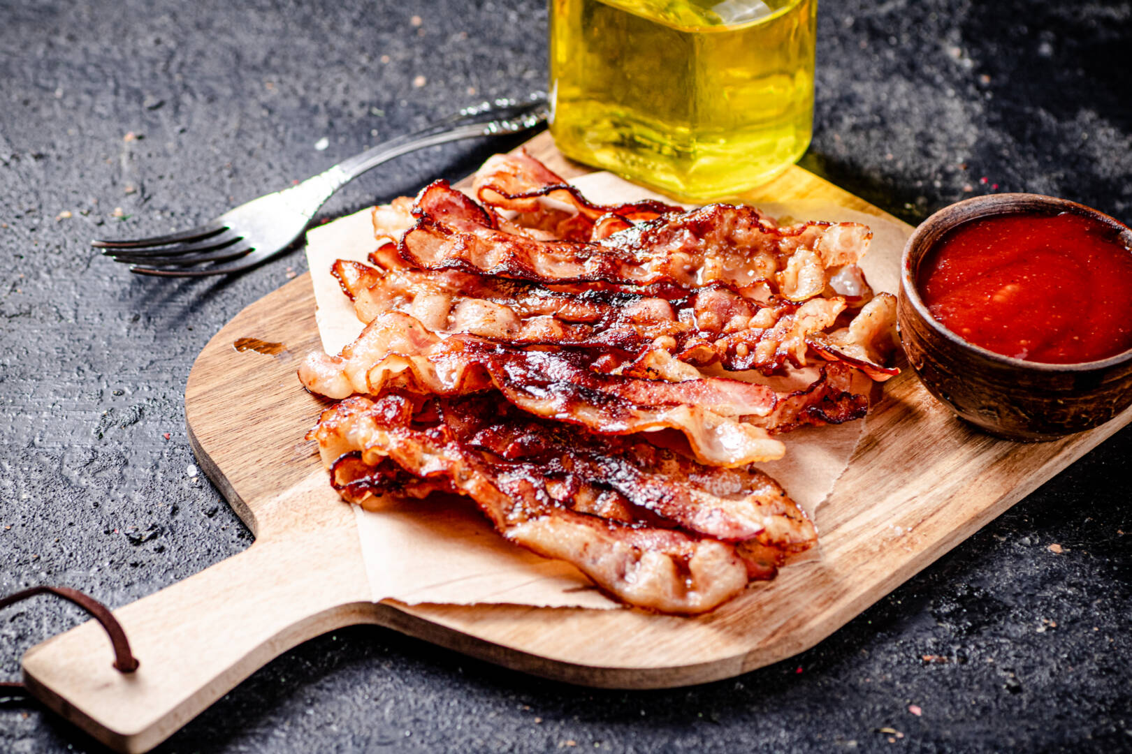 Pieces of fried bacon on a wooden cutting board. On a black background. High quality photo